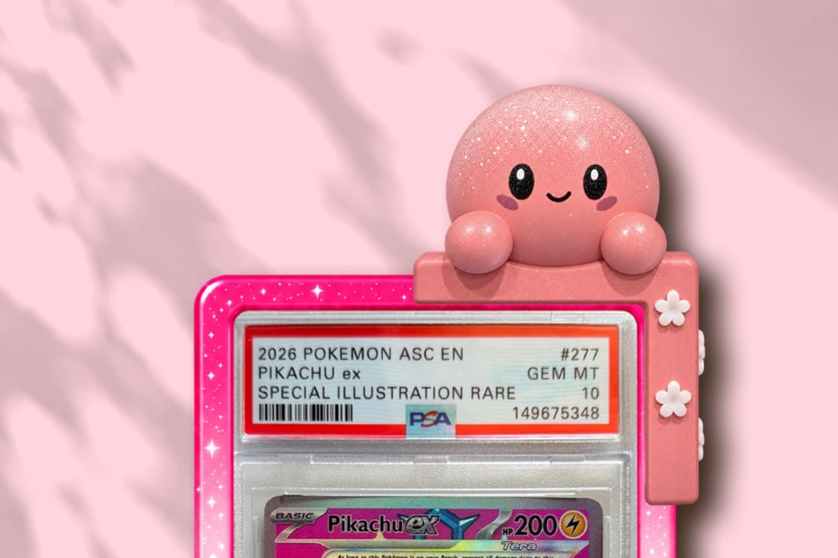 Momo clipped onto the corner of a graded Pikachu slab in a slab guard